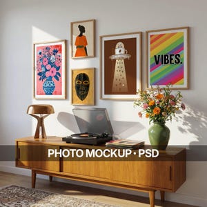 May include: A wooden media console with a record player, a gold lamp, and a green vase with flowers. Above, five framed art prints are displayed on the wall: a floral vase, a person in an orange dress, a mask, a coffee UFO, and rainbow text VIBES.