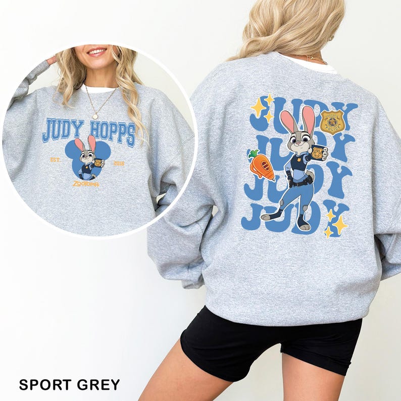 K&ouml;nnte beinhalten: Sportgraues Sweatshirt mit Judy Hopps aus Zoomania. Auf der Vorderseite steht "Judy Hopps" in Blau und Wei&szlig;. Auf der R&uuml;ckseite ist Judy Hopps mit Karotte und Abzeichen abgebildet, mit dem Schriftzug "Judy".