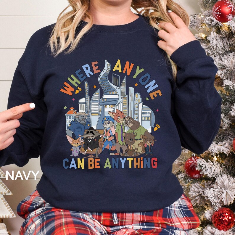 May include: Navy blue sweatshirt featuring a colorful graphic of a city skyline and various animal characters. The text "WHERE ANYONE CAN BE ANYTHING" is displayed in a rainbow font. The word "NAVY" is printed on the bottom left.
