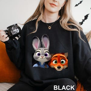 Może przedstawiać: Czarna bluza z nadrukiem Judy Hopps i Nicka Wilde z filmu Zwierzogr&oacute;d. Bluza ma okrągły dekolt i długie rękawy. Słowo "BLACK" jest wydrukowane na dole bluzy.