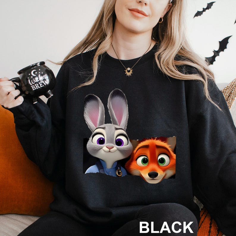 Może przedstawiać: Czarna bluza z nadrukiem Judy Hopps i Nicka Wilde z filmu Zwierzogr&oacute;d. Bluza ma okrągły dekolt i długie rękawy. Słowo "BLACK" jest wydrukowane na dole bluzy.