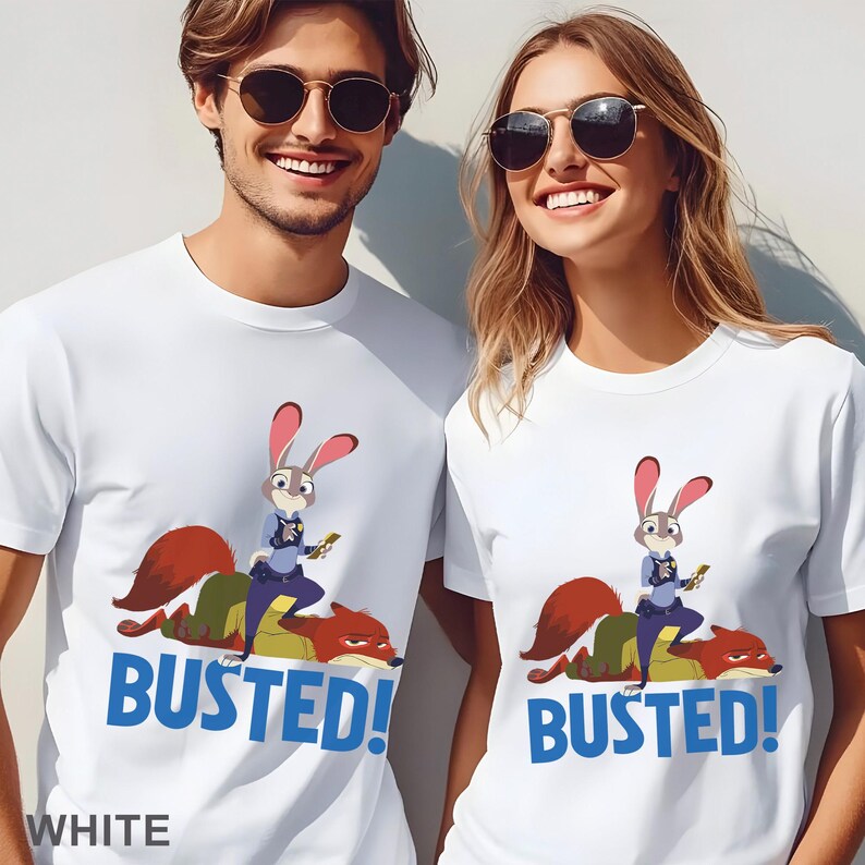 May include: White t-shirts with a cartoon image of a rabbit police officer and a fox, with the word "BUSTED!" in blue. The word "WHITE" is printed at the bottom of the shirt. The shirts are worn by two people.