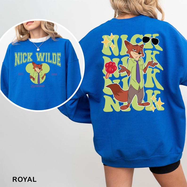 K&ouml;nnte beinhalten: K&ouml;nigsblaues Sweatshirt mit einem Cartoon-Fuchs-Charakter mit Sonnenbrille und Eis am Stiel. Auf der Vorderseite steht "Nick Wilde" in gr&uuml;ner Schrift. Auf der R&uuml;ckseite steht der gleiche Text im Retro-Stil. Ein lebendiges Kleidungsst&uuml;ck.