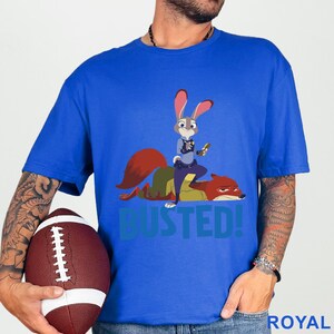 May include: Royal blue t-shirt with a cartoon image of a bunny police officer on top of a fox, with the word "BUSTED!" in teal. The shirt is made of a soft material.