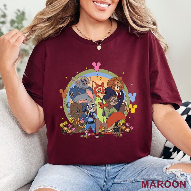 May include: Maroon t-shirt featuring a colorful graphic of characters from a popular animated movie. The design includes a rainbow, flowers, and Mickey Mouse silhouettes. The word "MAROON" is printed at the bottom.