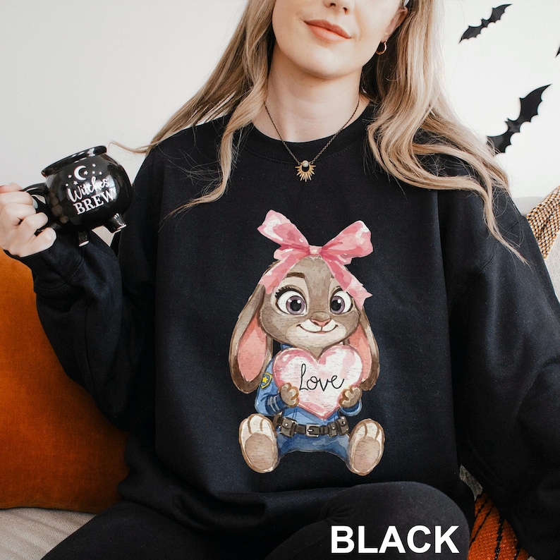 May include: Black sweatshirt with a cartoon bunny holding a heart-shaped sign that says "Love." The bunny has a pink bow and is wearing a police uniform. The word "BLACK" is printed at the bottom of the sweatshirt.