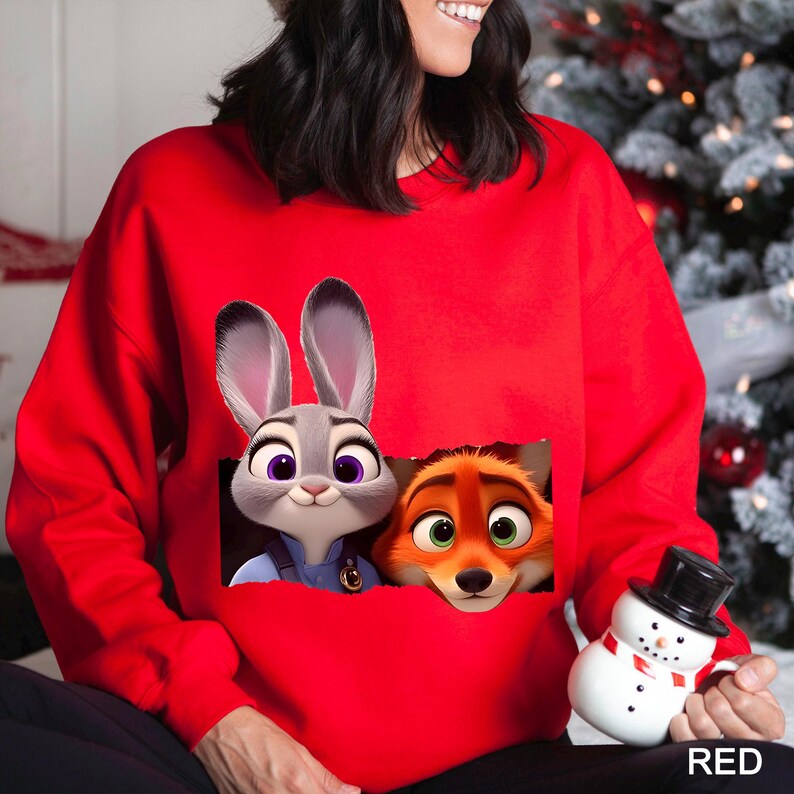 Może przedstawiać: Czerwona bluza z nadrukiem Judy Hopps i Nicka Wilde z filmu Zwierzogr&oacute;d. Postacie z kresk&oacute;wek wyglądają z kieszeni. Słowo "RED" jest wydrukowane na dole po prawej stronie.