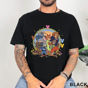 May include: Black t-shirt featuring a colorful graphic of cartoon animal characters, including a fox, rabbit, and lion, surrounded by flowers and stars. The design is set against a rainbow-colored background. The word "BLACK" is printed at the bottom.