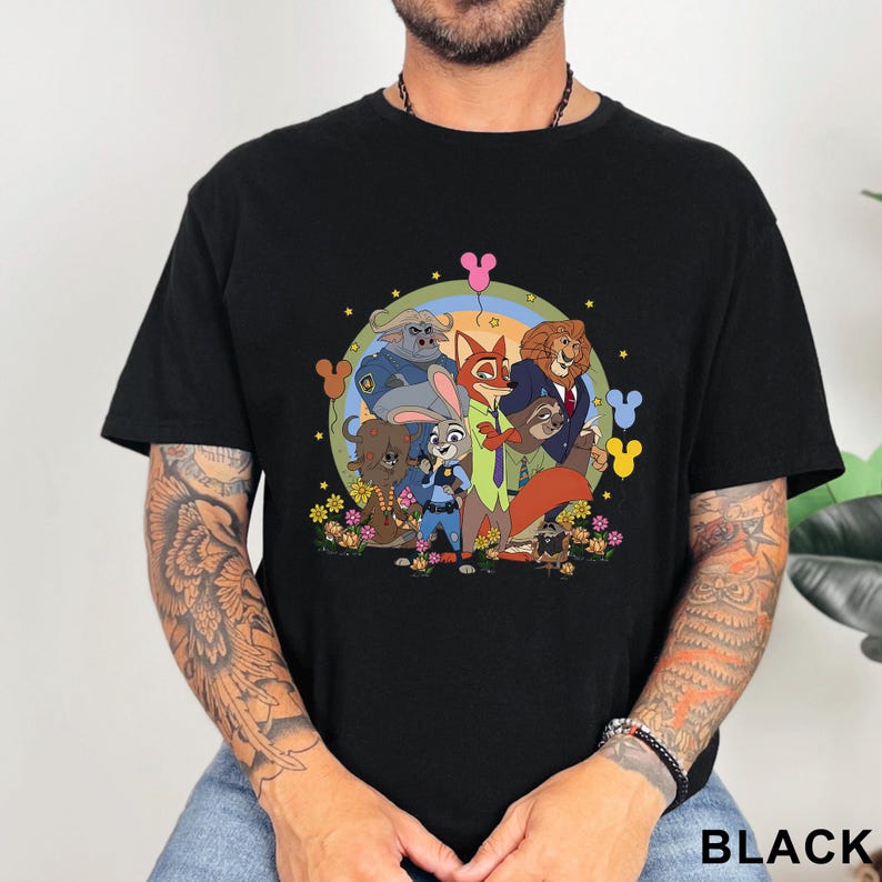 May include: Black t-shirt featuring a colorful graphic of cartoon animal characters, including a fox, rabbit, and lion, surrounded by flowers and stars. The design is set against a rainbow-colored background. The word "BLACK" is printed at the bottom.