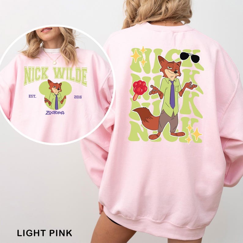 K&ouml;nnte beinhalten: Hellrosa Sweatshirt mit einer Cartoon-Illustration von Nick Wilde aus Zootopia. Auf der Vorderseite steht "Nick Wilde" und "Zootopia" mit einer Fuchs-Grafik. Auf der R&uuml;ckseite ist eine gr&ouml;&szlig;ere Nick Wilde-Grafik mit Sonnenbrille und Eis am Stiel.