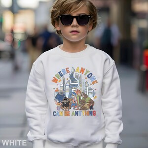 May include: White sweatshirt with a colorful graphic featuring cartoon characters and the text "WHERE ANYONE CAN BE ANYTHING". The design includes a cityscape and various animal figures.