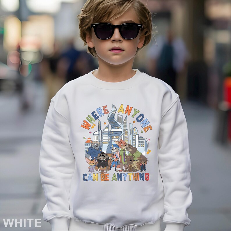 May include: White sweatshirt with a colorful graphic featuring cartoon characters and the text "WHERE ANYONE CAN BE ANYTHING". The design includes a cityscape and various animal figures.