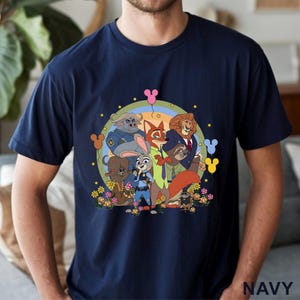 May include: Navy blue t-shirt featuring a colorful cartoon graphic of animal characters. The design includes a rainbow, flowers, and the word "NAVY" at the bottom. The shirt is a crew neck style.