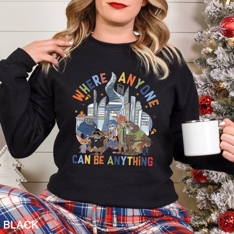 May include: Black crewneck sweatshirt featuring a colorful graphic of cartoon characters and the text "WHERE ANYONE CAN BE ANYTHING". The design includes a cityscape and various animal characters. The sweatshirt is a comfortable, casual style.