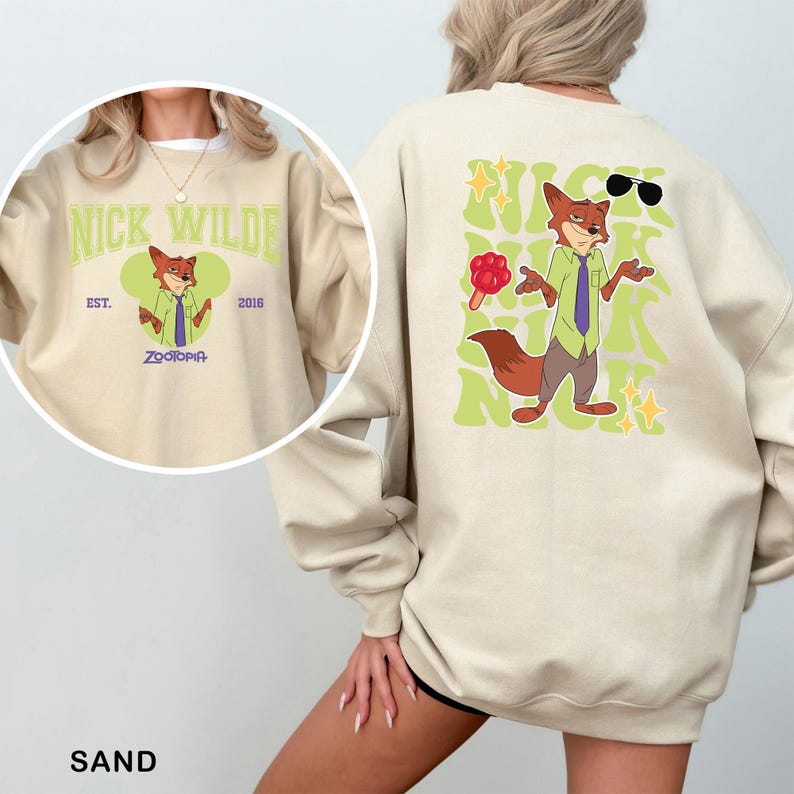K&ouml;nnte beinhalten: Sandfarbener Sweatshirt mit einem Cartoon-Fuchs-Charakter, Nick Wilde, aus Zootopia. Die Vorderseite hat ein kreisf&ouml;rmiges Design mit dem Bild und Text der Figur. Die R&uuml;ckseite zeigt eine gr&ouml;&szlig;ere Grafik des Fuchses mit Sonnenbrille und Text. Das Sweatshirt hat lange &Auml;rmel.