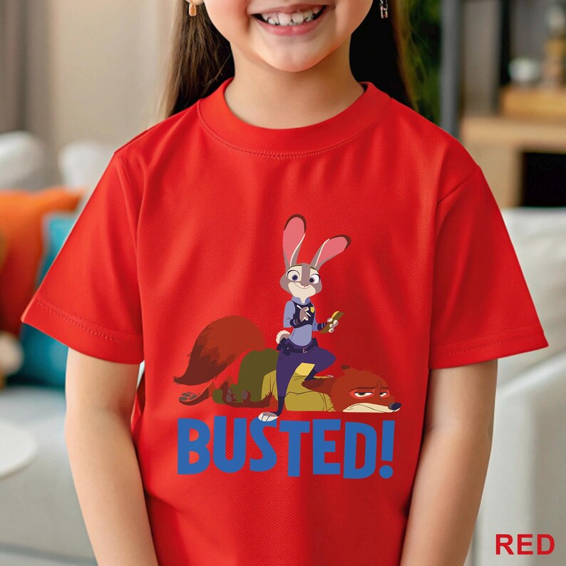 May include: A red t-shirt with a cartoon image of Judy Hopps and Nick Wilde from Zootropolis. The word "BUSTED!" is printed in blue below the characters. The word "RED" is printed in the bottom right corner of the t-shirt.