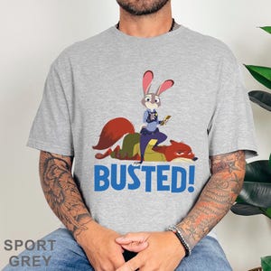 May include: Sport grey t-shirt with a cartoon image of a bunny police officer on a fox, and the blue text "BUSTED!". The shirt is made of a soft material.