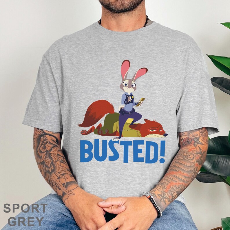May include: Sport grey t-shirt with a cartoon image of a bunny police officer on a fox, and the blue text "BUSTED!". The shirt is made of a soft material.