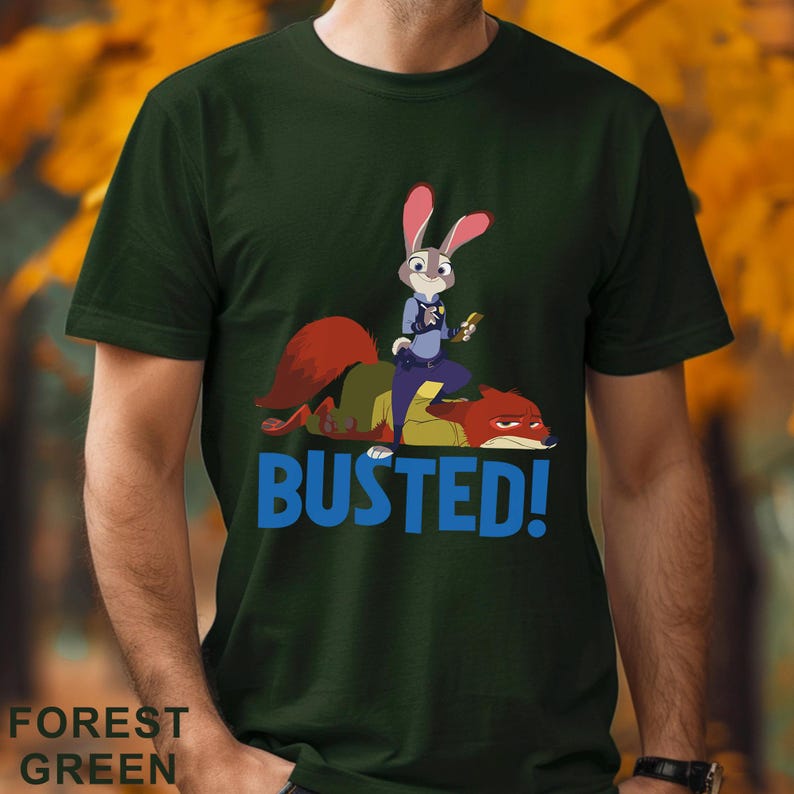 May include: Forest green t-shirt with a cartoon image of a rabbit police officer and a fox, with the word "BUSTED!" in blue. The rabbit is holding a small object. The shirt is a solid colour.