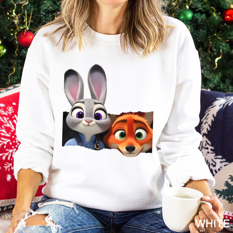 Może przedstawiać: Biała bluza z nadrukiem Judy Hopps i Nicka Wilde z Zwierzogrodu. Judy to szary kr&oacute;lik z fioletowymi oczami, a Nick to pomarańczowy lis z zielonymi oczami. Postacie wyłaniają się z efektu podartego papieru.