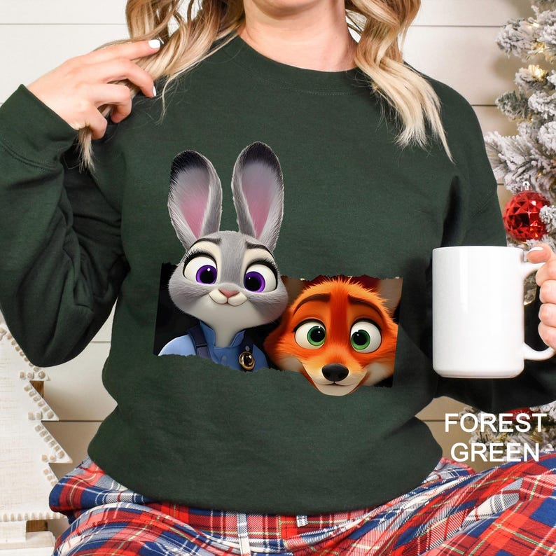 Może przedstawiać: Leśnozielona bluza z nadrukiem Judy Hopps i Nicka Wilde z Zwierzogrodu. Bluza ma okrągły dekolt i długie rękawy. W dłoni trzymany jest biały kubek. Tekst "FOREST GREEN" jest wydrukowany w prawym dolnym rogu.