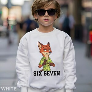 May include: White sweatshirt featuring a cartoon fox character wearing a green shirt with a floral pattern. The text "SIX SEVEN" is printed in black block letters below the character. The sweatshirt is worn by a child wearing sunglasses.