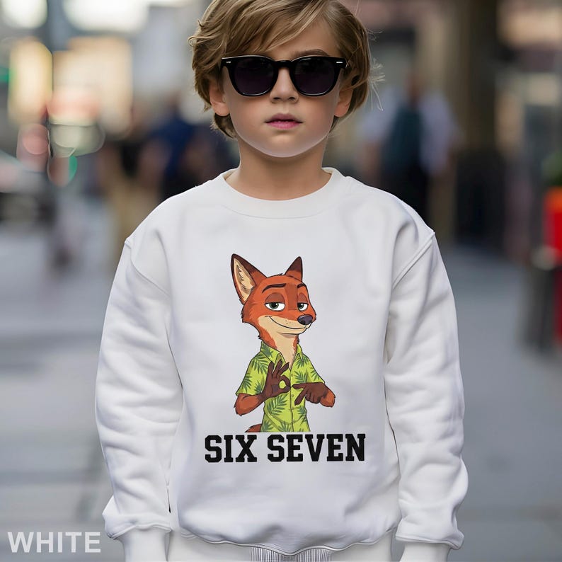 May include: White sweatshirt featuring a cartoon fox character wearing a green shirt with a floral pattern. The text "SIX SEVEN" is printed in black block letters below the character. The sweatshirt is worn by a child wearing sunglasses.