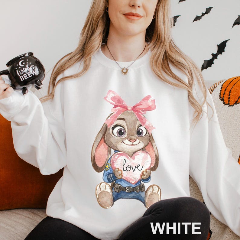 May include: White sweatshirt with a watercolour illustration of a bunny holding a heart with the word "Love". The bunny is in a police uniform and a pink bow. The word "WHITE" is printed at the bottom of the sweatshirt.