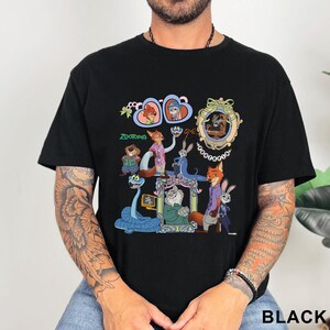 Puede incluir: Camiseta negra con un gr&aacute;fico colorido de personajes de la pel&iacute;cula animada Zootopia. El dise&ntilde;o incluye a Judy Hopps, Nick Wilde y otros personajes en marcos ornamentados. La palabra "Zootopia" est&aacute; impresa en verde.