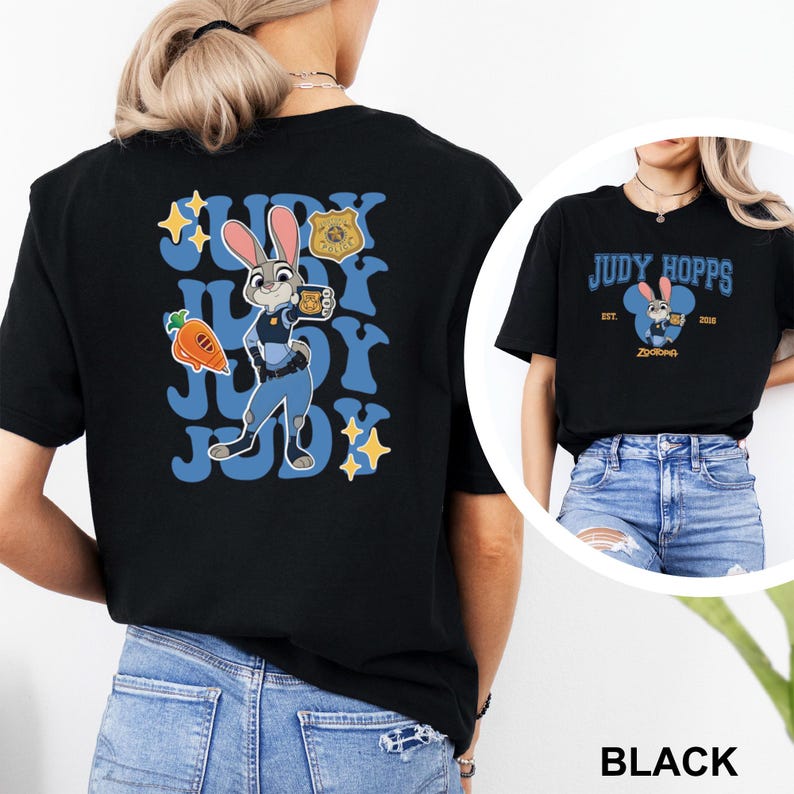May include: Black t-shirt featuring a cartoon image of Judy Hopps from Zootopia. The design includes the text "JUDY HOPPS" in blue, a carrot, a police badge, and stars. The shirt is shown on a person wearing blue jeans.