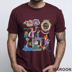 Puede incluir: Camiseta granate con un gr&aacute;fico colorido de personajes de la pel&iacute;cula animada Zootopia. El dise&ntilde;o incluye retratos enmarcados de varios personajes animales, con la palabra "ZOOTOPIA" en verde.