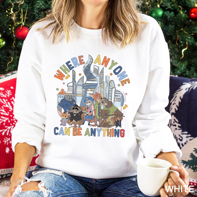 May include: White sweatshirt featuring a colorful graphic of a city skyline and cartoon characters. The text "WHERE ANYONE CAN BE ANYTHING" is displayed above the characters. The sweatshirt is a crew neck style.