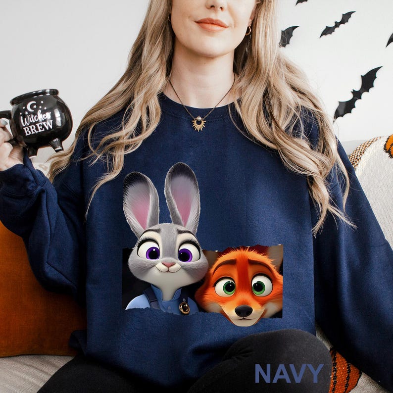 Może przedstawiać: Granatowa bluza z nadrukiem Judy Hopps i Nicka Wilde z filmu Zwierzogr&oacute;d. Bluza ma okrągły dekolt i długie rękawy. Słowo "NAVY" jest wydrukowane na dole. Obraz jest w stylu kresk&oacute;wki.