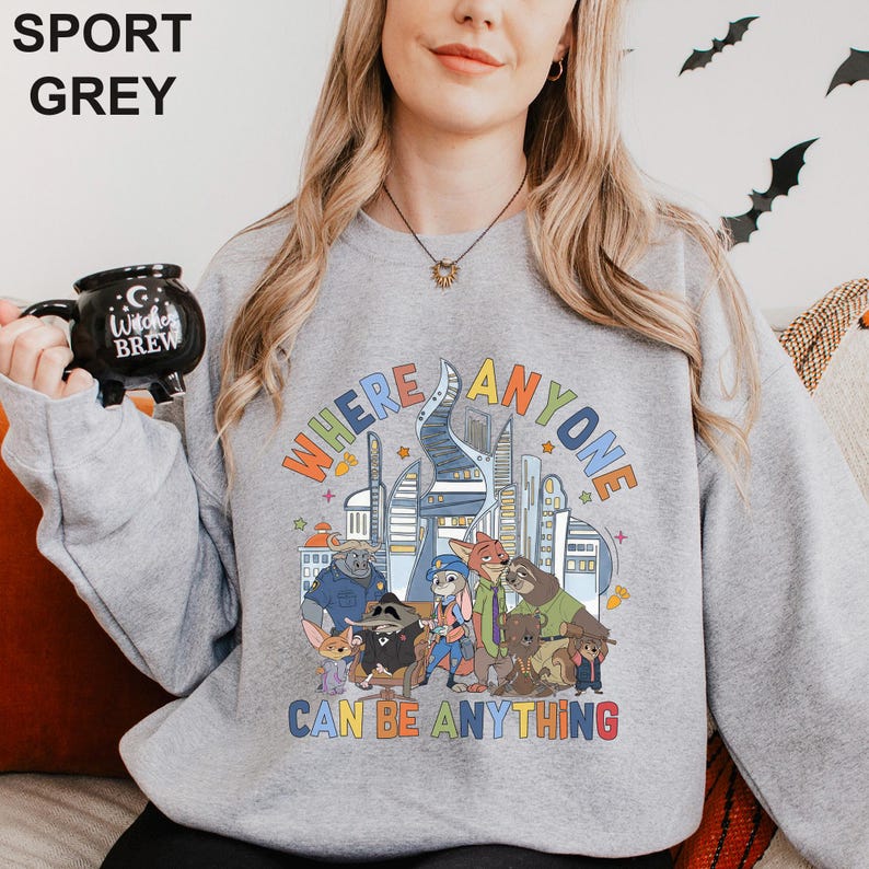 May include: Sport grey sweatshirt with a colorful graphic featuring cartoon characters and the text "WHERE ANYONE CAN BE ANYTHING". The sweatshirt is a crew neck style.