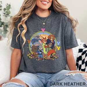 May include: Dark heather gray t-shirt featuring a colorful cartoon graphic of characters from Zootopia. The design includes Judy Hopps, Nick Wilde, and other characters, surrounded by a rainbow and flowers. The text "DARK HEATHER" is printed at the bottom.