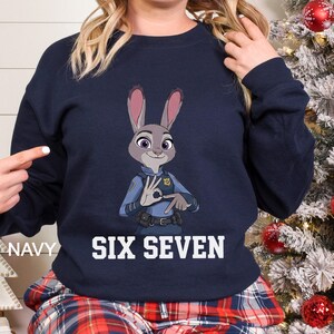 May include: Navy blue sweatshirt featuring a cartoon image of Judy Hopps from Zootopia, in a police uniform, making a hand gesture. The words "SIX SEVEN" are printed in white block letters below the image. The word "NAVY" is printed on the left side.