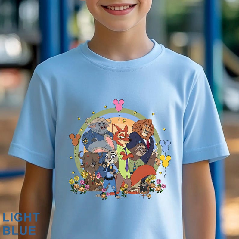 May include: Light blue t-shirt featuring a colorful graphic of animated animal characters. The design includes a fox, rabbit, lion, and other characters, surrounded by flowers and balloons. The text "LIGHT BLUE" is at the bottom.