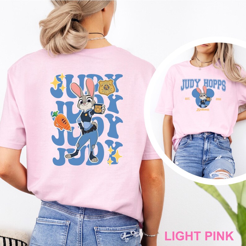 May include: Light pink t-shirt featuring Judy Hopps from Zootopia. The back of the shirt has a blue design with Judy Hopps in her police uniform, a carrot, and the words "Judy" repeated. The front of the shirt has the words "Judy Hopps" and a cartoon image of Judy.