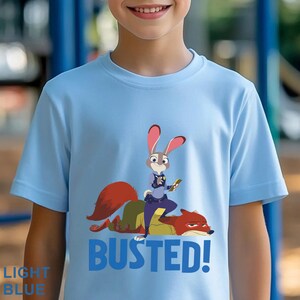 May include: Pale blue t-shirt with a cartoon image of a rabbit police officer and a fox, with the word "BUSTED!" in blue. The shirt also has the words "LIGHT BLUE" in the bottom left corner.
