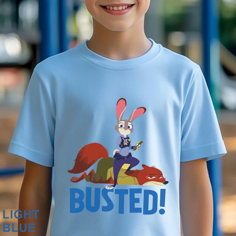 May include: Pale blue t-shirt with a cartoon image of a rabbit police officer and a fox, with the word "BUSTED!" in blue. The shirt also has the words "LIGHT BLUE" in the bottom left corner.