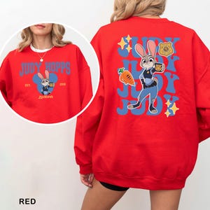 K&ouml;nnte beinhalten: Rotes Sweatshirt mit Judy Hopps aus Zootopia. Die Vorderseite hat ein blaues Design mit dem Text "JUDY HOPPS" und einem Cartoon-Bild von Judy. Die R&uuml;ckseite zeigt ein gr&ouml;&szlig;eres Bild von Judy Hopps mit Text und Sternen.