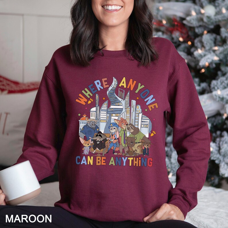 May include: Maroon sweatshirt with the text "WHERE ANYONE CAN BE ANYTHING" in colorful letters. The graphic features cartoon animals and a cityscape. The sweatshirt is a crew neck style.