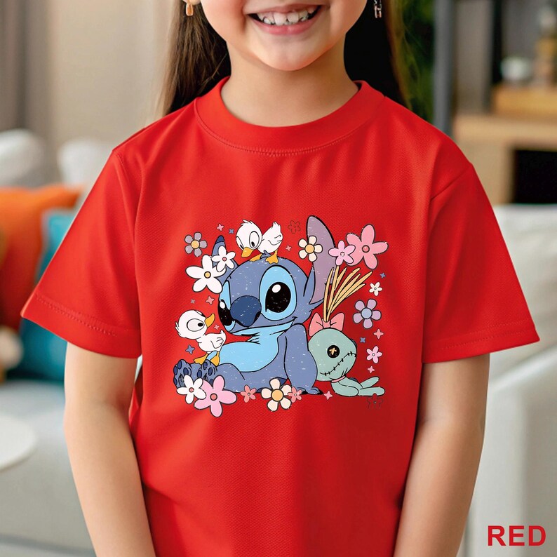 K&ouml;nnte beinhalten: Rotes T-Shirt mit einem Cartoon-Motiv von Stitch, umgeben von Blumen und Enten. Eine gr&uuml;ne Puppe mit rosa Schleife ist ebenfalls abgebildet. Das Wort "RED" ist unten rechts aufgedruckt. Kinder-T-Shirt.