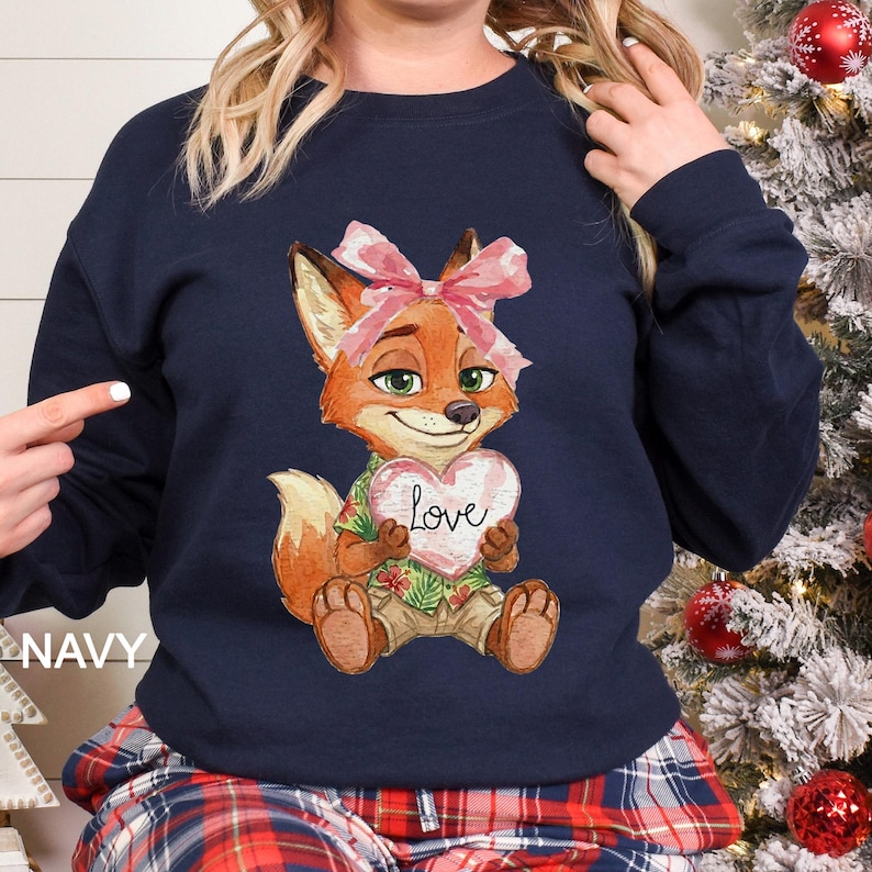 May include: Navy blue sweatshirt with a cartoon fox holding a heart that says "Love". The fox has orange fur and a pink bow. The fox is wearing a Hawaiian shirt. The word "NAVY" is printed on the left side of the sweatshirt.