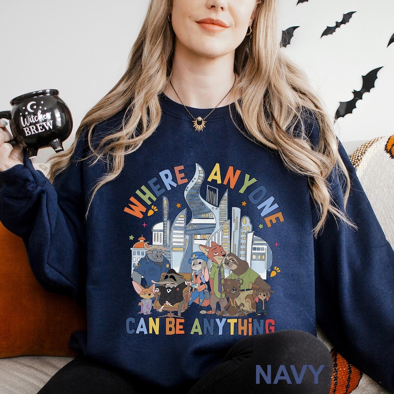 May include: Navy blue sweatshirt with a colorful graphic featuring cartoon characters and the text "WHERE ANYONE CAN BE ANYTHING." The design includes a cityscape and various animal figures. The word "NAVY" is printed at the bottom.