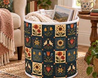 May include: A cylindrical fabric storage basket featuring a repeating grid pattern of floral motifs, sunflowers, birds, and hearts in shades of red, yellow, blue, and green on a dark blue background, with a white quilted rim and interior lining.