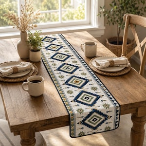 May include: A long rectangular table runner featuring a repeating geometric diamond pattern in shades of navy blue, olive green, and cream. The runner has a dark border and is centered on a wooden table, showcasing a symmetrical design.