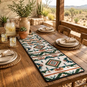 May include: A long rectangular table runner featuring a repeating geometric pattern in shades of green, orange, and brown on a cream background. The runner is quilted with a dark border and is placed on a wooden table with plates and glasses.