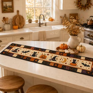 May include: A rectangular fabric table runner featuring a repeating pattern of black cats, orange pumpkins, witch hats, bats, and crescent moons on a cream background, bordered by black and orange squares with small star and leaf motifs.