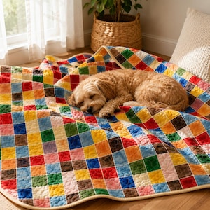 Peut inclure: Une couverture matelassée présentant un motif de grille multicolore composé de petits carrés dans des tons de rouge, bleu, jaune, vert et marron. Le tissu présente une texture piquée visible et une bordure de couleur claire.